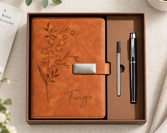 Puede incluir: Un cuaderno color canela con un grabado floral y el nombre Fuego, con un cierre magnético plateado. El cuaderno se presenta en una caja de regalo marrón junto a un bolígrafo de tinta negra y un recambio de metal plateado en una bandeja.