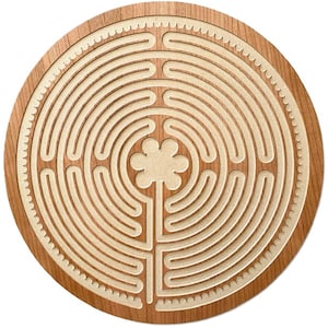 May include: A circular wooden plaque featuring a light-colored, recessed labyrinth pattern carved into a darker wood grain surface. The center of the maze displays a six-petaled flower shape, and the outer edge is bordered by a scalloped design.