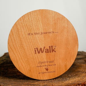 May include: A round, wooden item with the text "It's the journey...." and "iWalk" engraved on it. The item also includes the text "iSpiritual made in Big Bear CA" and a paw print symbol. The wood has a light brown color.