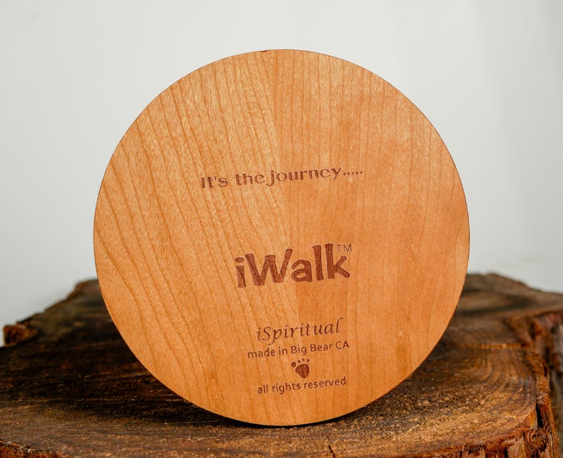 May include: A round, wooden item with the text "It's the journey...." and "iWalk" engraved on it. The item also includes the text "iSpiritual made in Big Bear CA" and a paw print symbol. The wood has a light brown color.