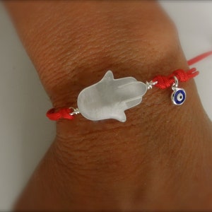 May include: A red string bracelet with a white hamsa hand charm and a blue evil eye charm.