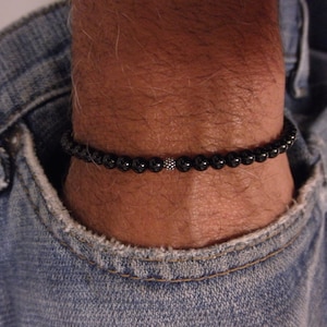 Puede incluir: Un brazalete de cuentas negras con un acento de cuentas plateadas.