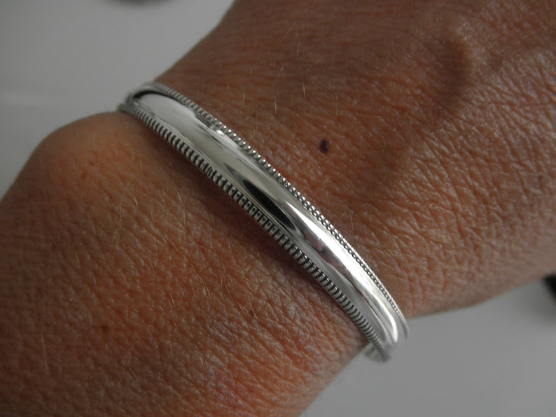 May include: A silver bangle bracelet with a beaded edge.