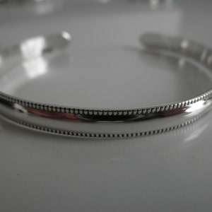 May include: A silver bangle bracelet with a beaded edge.