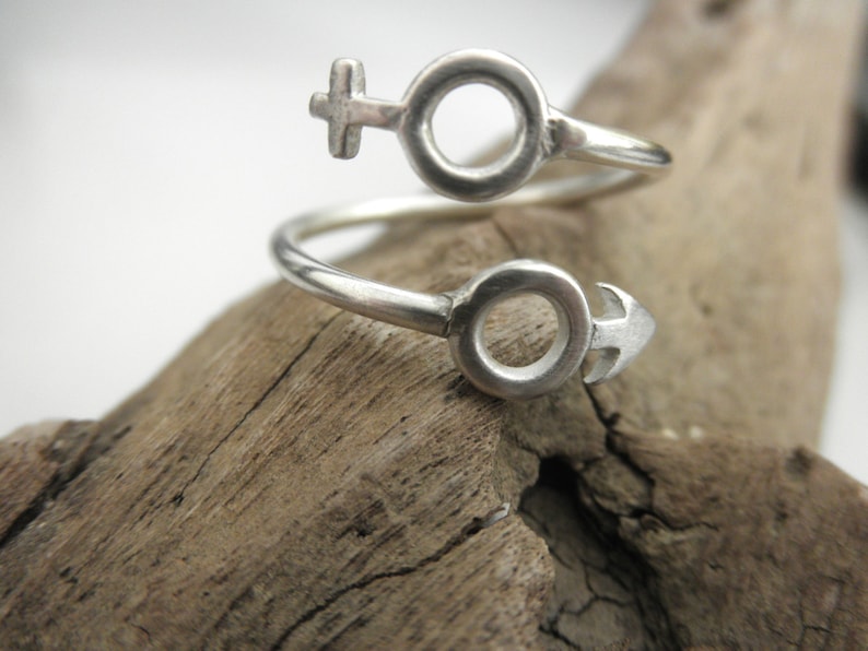 May include: A silver ring with a twisted design featuring the male and female symbols.
