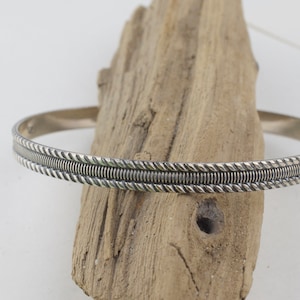 May include: A silver bangle bracelet with a braided design.