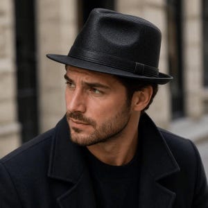 Puede incluir: Un sombrero fedora negro con una superficie texturizada y granulada, que incluye una banda negra a juego alrededor de la copa. El sombrero presenta una copa pellizcada y un ala estructurada, ofreciendo una silueta clásica sobre la cabeza.