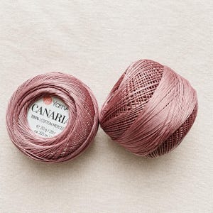 Op de afbeelding: Twee bollen oudroze gemerceriseerd katoengaren. Eén bol heeft een wit label met de tekst YarnArt CANARIA 100% COTTON MERCERIZED e 20 g / 20 r ca. 203 m. Het garen heeft een gladde, licht glanzende textuur en is in een compacte bol gewikkeld.