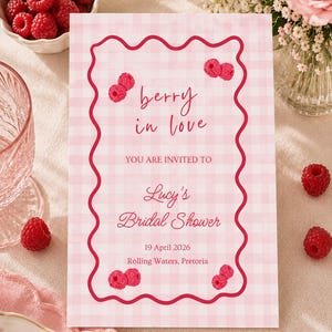 Puede incluir: Una tarjeta de invitación rectangular con patrón de cuadros vichy rosa claro y blanco, borde ondulado rosa oscuro e ilustraciones de frambuesas. El texto dice: berry in love, YOU ARE INVITED TO, Lucy's Bridal Shower, 19 April 2026, Rolling Waters, Pretoria.