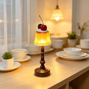 Lámpara de mesa pequeña con forma de pudín de crema, adornada con cerezas y galletas, con base de madera de estilo retro. Luz nocturna cálida y encantadora con diseño de postre.