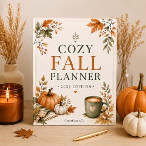 May include: A hardback planner with a cream-coloured cover featuring the text COZY FALL PLANNER 2026 EDITION. The design includes watercolour illustrations of orange and white pumpkins, autumn leaves, and a green mug with a heart icon.