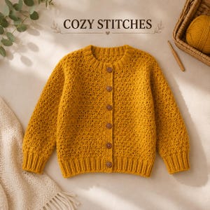 Könnte beinhalten: Eine senfgelbe, langärmelige Strickjacke mit Rundhalsausschnitt, gerippten Bündchen und Saum sowie sechs braunen Knöpfen auf der Vorderseite. Über dem Kleidungsstück steht der Text COZY STITCHES, ergänzt durch ein Wollknäuel und eine Häkelnadel.