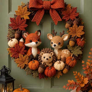 May include: A circular wreath made of woven twigs, decorated with crocheted autumn leaves in shades of red, orange, and green, crocheted acorns, and small pumpkins. A large crocheted orange bow sits at the top. Three crocheted animals, a fox, a deer, and a hedgehog, are positioned in the center.