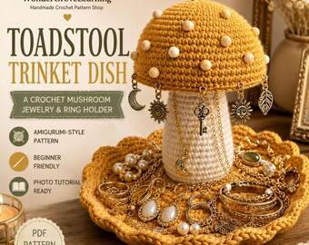 May include: A crochet toadstool trinket dish featuring a mustard yellow mushroom cap with white beads, a cream-coloured stem, and a scalloped mustard yellow base. The cap is adorned with dangling metal charms including a moon, sun, and key.