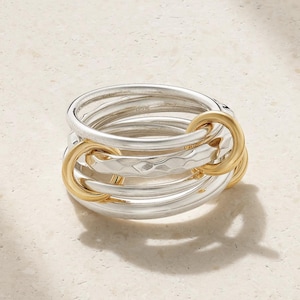 May include: A multi-band ring featuring several interlocking silver bands and two smaller gold-toned rings. One of the silver bands has a hammered, textured finish, while the others are smooth and polished. The ring is marked with 925.