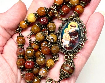 May include: A brown and gold rosary with a saint medal and a crucifix. The beads are made of agate and the metal accents are antique gold.