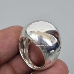May include: A wide, polished silver ring with a smooth, rounded, and domed surface. The metal has a reflective, high-shine finish with subtle organic contours. The text ShreeJaipurSilverIND is visible on the side of the band.