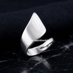 Op de afbeelding: Een gepolijste zilveren ring met een open, wikkelontwerp en een breed, glad, bladachtig middelpunt dat uitloopt in een punt. Het metalen oppervlak is reflecterend en helder, met een strakke, doorlopende curve die de ringband vormt.