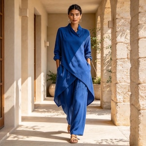 May include: A vibrant blue long-sleeved tunic with a wrap-style front and asymmetrical hemline, paired with matching wide-leg trousers. The ensemble features a soft, textured fabric, a high collar, and deep side pockets, creating a cohesive look.