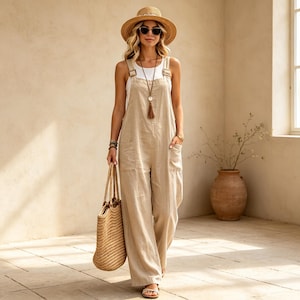 May include: A beige linen overall jumpsuit with wide legs and side pockets, worn over a white tank top. The outfit includes a straw sun hat, dark sunglasses, a long necklace with a brown tassel pendant, and a large woven straw tote bag.