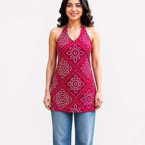 May include: A magenta halter top featuring a white geometric pattern of repeating floral motifs and zigzag lines arranged in a diamond grid, paired with light blue denim jeans. The top has a V-neckline and a sleeveless cut.