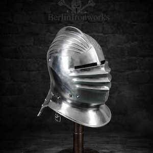 May include: A polished silver metal armet helmet featuring a rounded crown with vertical fluting, a hinged visor with horizontal sight slits, and a flared gorget neck guard. The text BerlinIronworks is visible above the helmet.