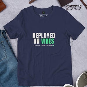 Könnte beinhalten: Ein marineblaues Kurzarm-T-Shirt mit dem weißen und hellgrünen Text "DEPLOYED ON VIBES" und dem Befehlszeilencode "$ git push --force --no-regrets", der mittig auf der Brust aufgedruckt ist.
