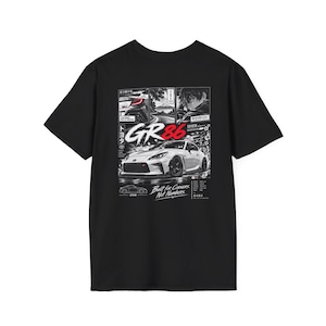 May include: A black short-sleeve t-shirt featuring a graphic print of a white Toyota GR86 car. The design includes manga-style panels, Japanese text, cherry blossoms, and the phrases GR86 and Built for Corners, Not Numbers in white and red.