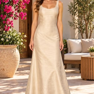 May include: A floor-length, sleeveless champagne-coloured gown featuring a scoop neckline and a fitted bodice that transitions into a flowing, A-line skirt. The fabric has a subtle, shimmering texture throughout the entire garment.