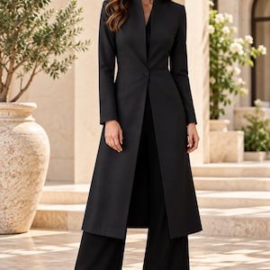 May include: A long-line black blazer featuring a high stand-up collar, long sleeves, and a single-button closure at the waist. The garment is paired with matching black wide-leg trousers and black pointed-toe heels, creating a monochromatic ensemble.