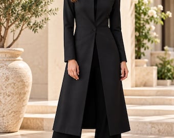 Puede incluir: Una chaqueta larga de color negro con cuello alto, mangas largas y un cierre de un solo botón en la cintura. La prenda se combina con pantalones negros de pierna ancha a juego y zapatos de tacón negros con punta afilada.