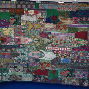 Puede incluir: Un tapiz o colcha rectangular compuesto por numerosos segmentos de tela de patchwork en varios tonos de verde, rojo, azul y rosa. El textil presenta intrincados patrones de bordado floral, cachemir y geométricos en toda la superficie.