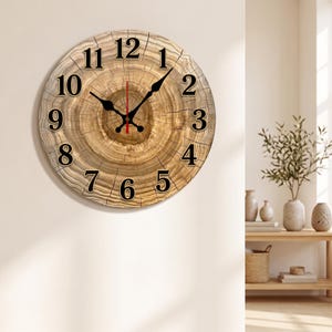 May include: A round wall clock featuring a printed wood grain pattern that mimics the appearance of a tree cross-section. The clock face displays black Arabic numerals from 1 to 12, with black hour and minute hands and a thin red second hand.