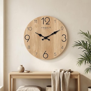 May include: A round wall clock with a light oak wood grain finish, featuring large black Arabic numerals from 1 to 12. The clock has black metal hands and the text "act The Ultimate clock QUARTY LTD" printed in black below the 12 o'clock position.