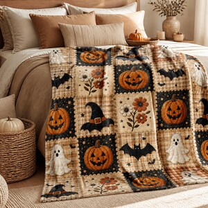 May include: A soft throw blanket featuring a patchwork design with alternating squares. The pattern includes orange jack-o'-lanterns, white ghosts, black bats, black witch hats, and clusters of orange and white flowers on plaid and dark backgrounds.