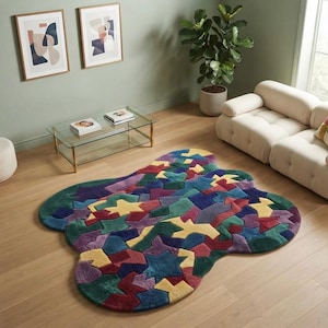 May include: An irregularly shaped area rug featuring a vibrant, multi-colored geometric pattern composed of interlocking shapes in shades of deep blue, forest green, mustard yellow, and burgundy, laid flat on a light-colored wooden floor.
