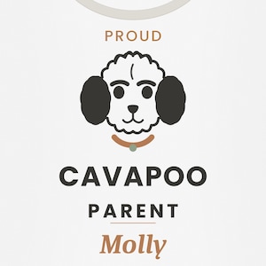 May include: A white t-shirt featuring a graphic of a stylized Cavapoo dog face with black ears, a brown collar, and the text PROUD CAVAPOO PARENT Molly in black and brown lettering. The design is centered on the chest of the garment.