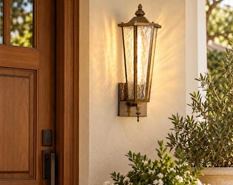 May include: A wall-mounted outdoor lantern with a metallic bronze finish and a tapered hexagonal frame. The fixture features textured, water-glass panels that diffuse a warm, vertical light, secured by a decorative finial at the base.