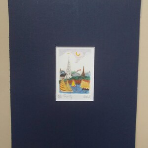 May include: A colorful watercolor painting of a small town with a church steeple and sailboats in the water. The painting is framed in a dark blue mat.