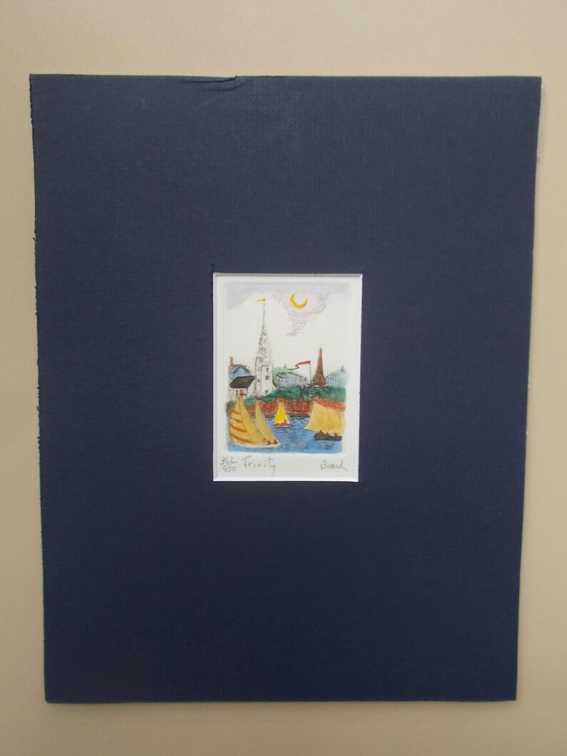 May include: A colorful watercolor painting of a small town with a church steeple and sailboats in the water. The painting is framed in a dark blue mat.