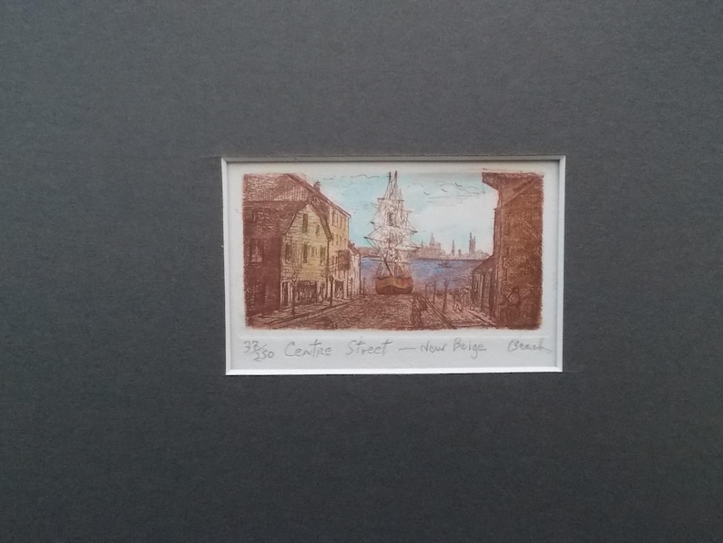 以下が含まれることがあります： 建物と帆船のある港の風景の額入りプリント。アートワークは茶色の色合いで、青い空と水があります。「33/50 Centre Street - New Paige Beach」というテキストが下にあります。