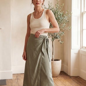 Peut inclure: Un débardeur côtelé de couleur crème associé à une jupe portefeuille mi-longue vert sauge. La jupe présente une fermeture à nouer sur le côté à la taille, un ourlet droit et un design simple et épuré qui tombe sous les genoux dans un ton vert.