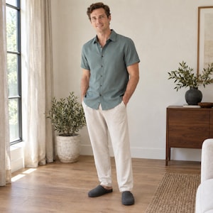May include: A short-sleeved button-down shirt in a muted sage green color paired with light beige trousers and dark gray slip-on slippers. The shirt features a classic collar and a full front button placket with matching buttons.