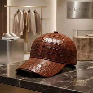 Pode incluir: Um boné de beisebol castanho com um padrão texturizado de pele de crocodilo. O boné apresenta uma coroa estruturada, uma aba curva e um pequeno botão no centro do topo. A superfície tem um acabamento brilhante em tons de castanho escuro.