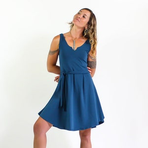 May include: A woman wearing a teal blue sleeveless dress with a tie belt. The dress has a V-neckline and a flowy skirt.