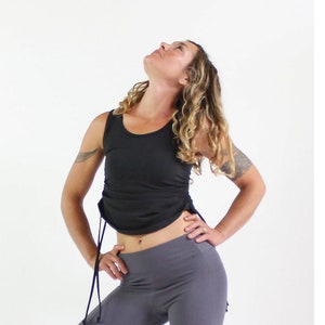 May include: A woman wearing a black tank top with a drawstring detail and gray leggings. The tank top has a scoop neck and the leggings are fitted.