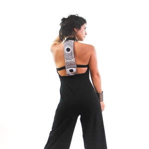 May include: A black jumpsuit with a wide-leg silhouette and a geometric patterned back detail. The jumpsuit has a halter neckline and a low back.