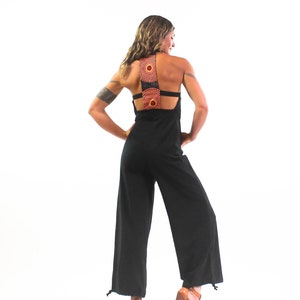 May include: A black jumpsuit with a wide-leg silhouette and a unique back design featuring two circular cutouts with orange and red patterned fabric.