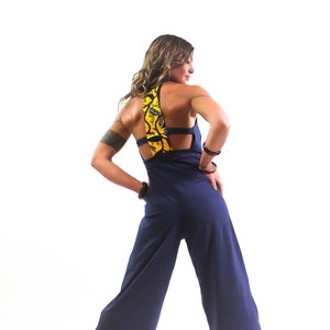 May include: A navy blue jumpsuit with a yellow and black patterned fabric detail on the back. The jumpsuit has a wide leg and a relaxed fit.