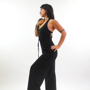 May include: A black sleeveless jumpsuit with a wide leg. The jumpsuit has a scoop neck and a tie at the waist.